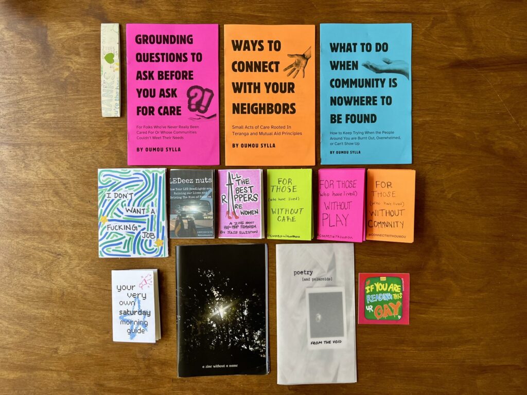 Zwölf Zines von Zines4Queers liegen auf einem Holztisch.