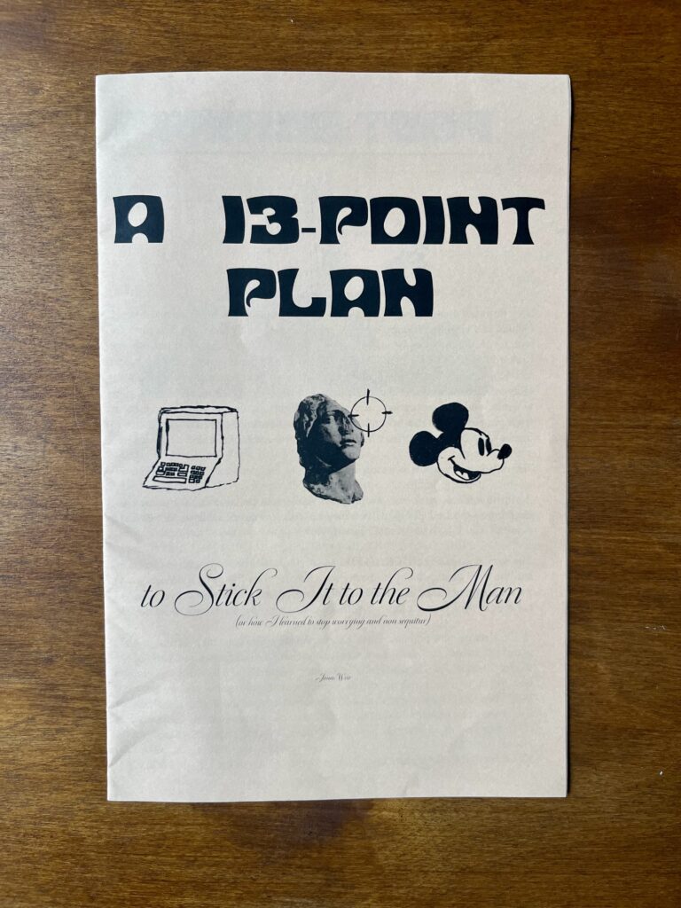 Auf einer dunklen Holzoberfläche liegt das A5 große Zine "A 13 Point Plan".