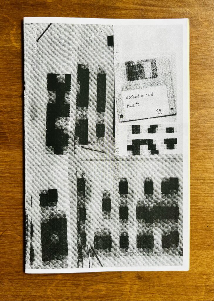 Auf einer Holzoberfläche liegt Issue 1 des s/w-Zines "Etched in Sand".