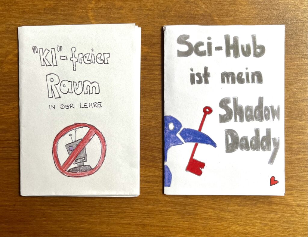 Zwei Minizines liegen nebeneinander auf einer dunkelbraunen Holzoberfläche. Das linke Zine hat den Titel "KI-freier Raum in der Lehre" und das rechte Zine den Titel "Sci-Hub ist mein Shadow Daddy".