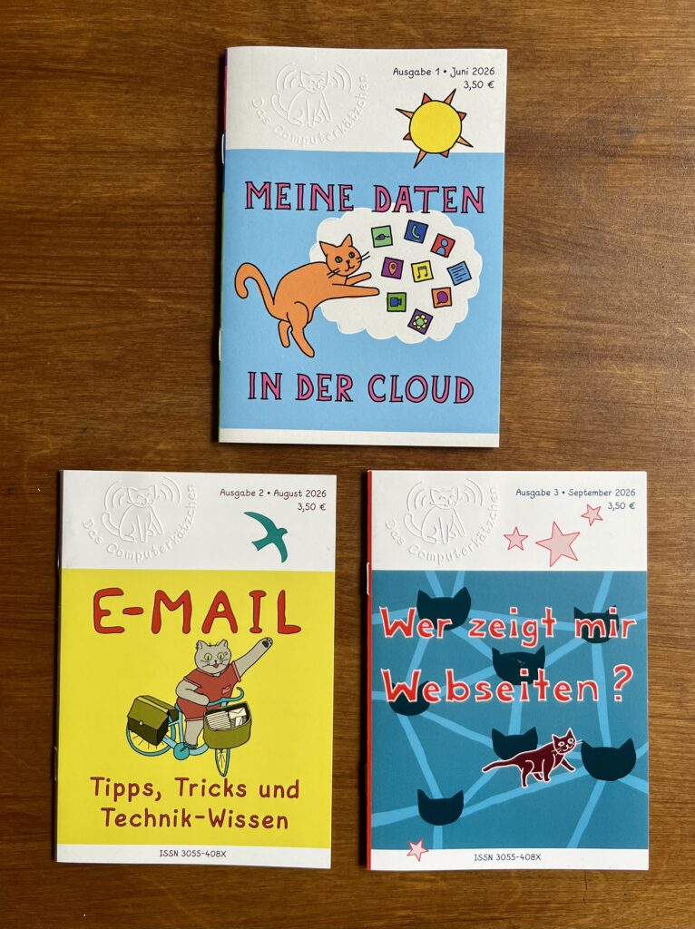 Foto der ersten drei Ausgaben des "Computerkätzchens": "Meine Daten in der Cloud", "E-Mail" und "Wer zeigt mir Webseiten", die auf einer dunklen Holzoberfläche liegen.